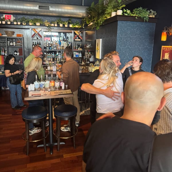 Patrons socialize around a high-top table with bottles and a bar in the background at Luna & The Bear.