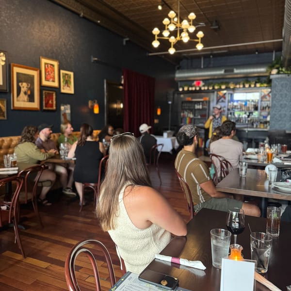 Diners seated at tables in Luna & The Bear, with a bar and bartender in the background.