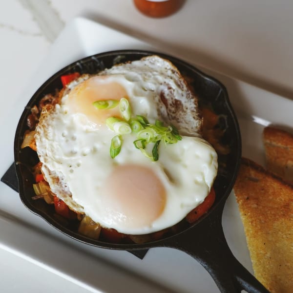 Skillet breakfast with two fried eggs, sautéed vegetables, and a side of toast at Luna & The Bear.