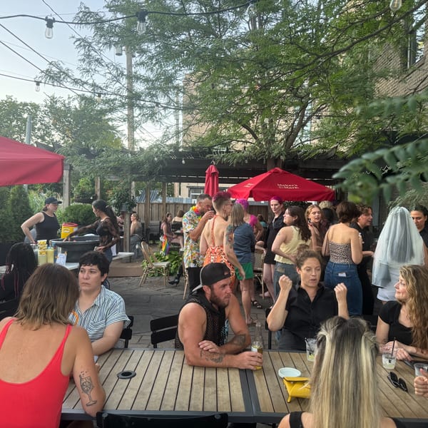 Patrons socialize on the Luna & The Bear outdoor patio under string lights and red umbrellas.