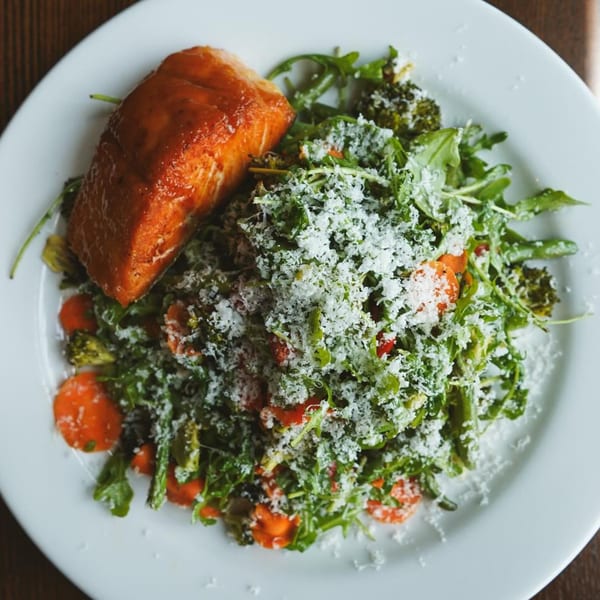 New-American salmon dish with a side of greens, carrots, broccoli, and grated cheese.