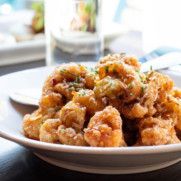 Crispy fried cauliflower bites, garnished with sesame seeds and chives, on a white plate at Luna & The Bear.