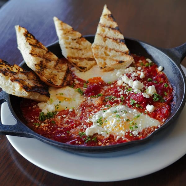 Shakshuka with baked eggs, tomato sauce, feta, and grilled bread in a cast iron skillet.