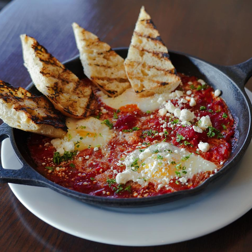 Shakshuka with baked eggs, tomato sauce, feta, and grilled bread in a cast iron skillet.