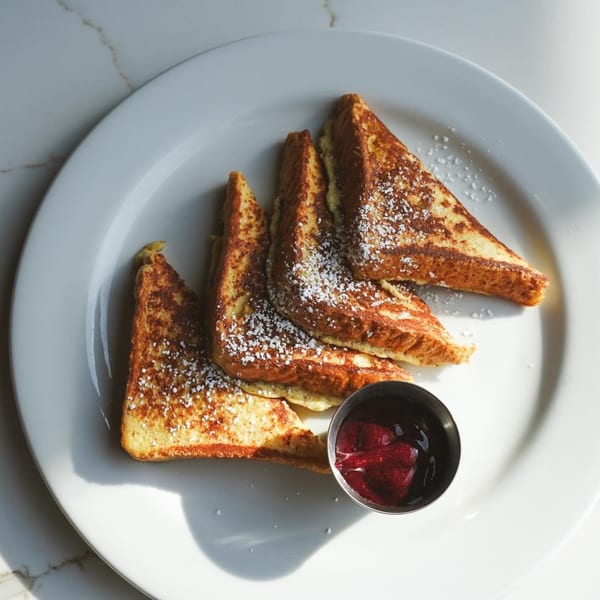 Golden French toast triangles dusted with powdered sugar, served with berry compote on a white plate.
